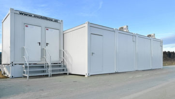 Containeranlage bestehend aus vier Stück Baucontainer in der Farbe RAL 9002 Grauweiß. Sanitärcontainer neben der Containeranlage auf einem Fäkalientank mit Podest und Treppen positioniert.