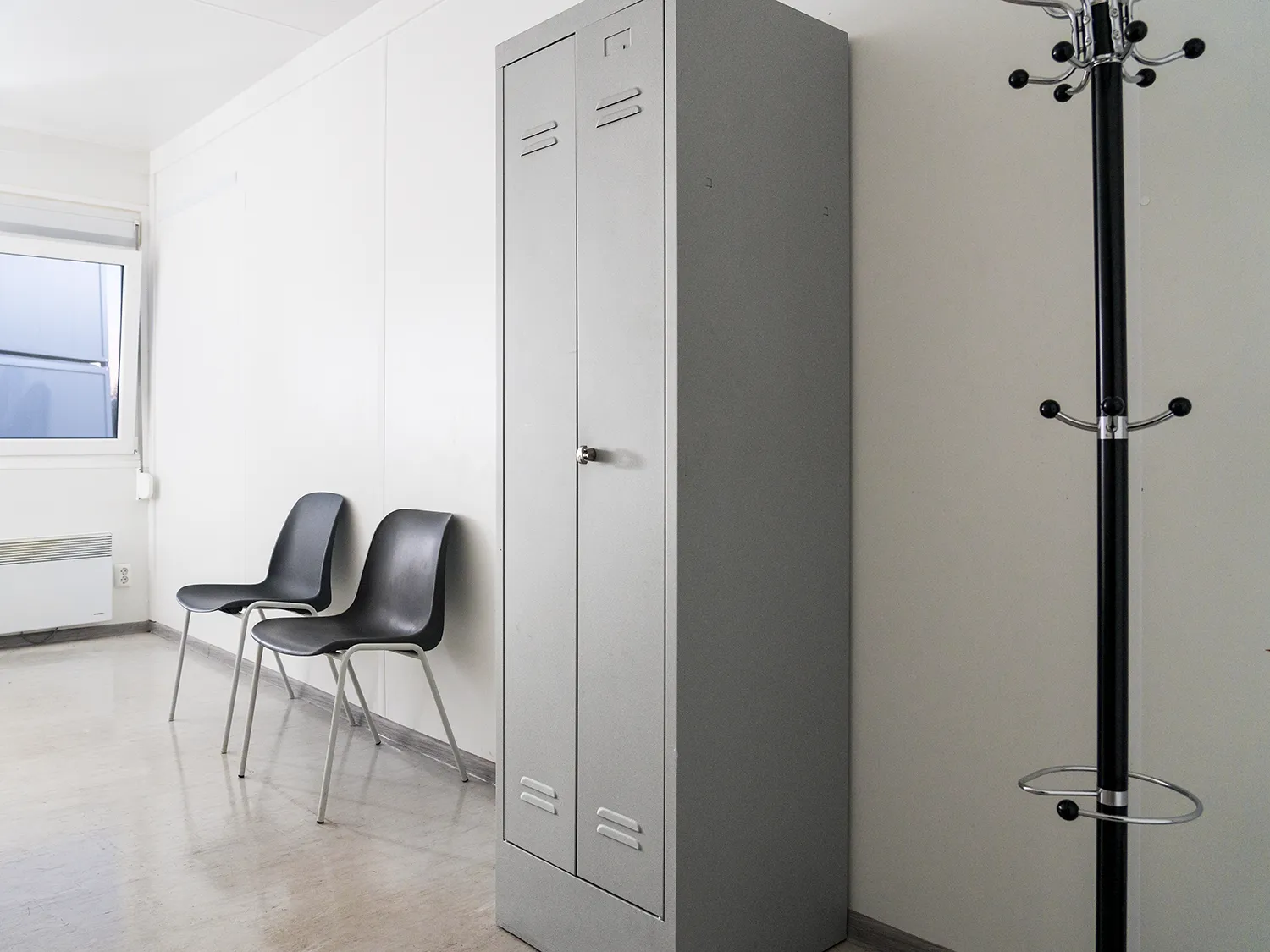 grauer Spind als Teil der Ausstattung eines Mannschaftscontainer zur miete mit zwei Stapelstühlen und einem Kleiderständer daneben.