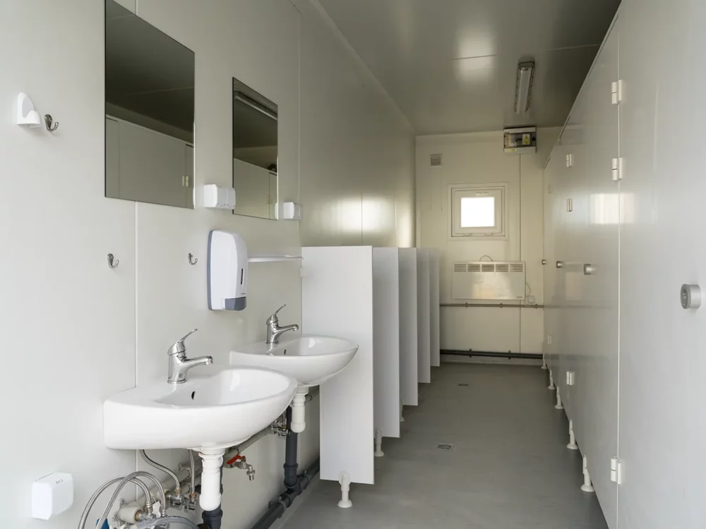 Mietbarer Sanitärcontainer von innen fotografiert mit zwei Waschbecken, Urinalen samt Schamwänden sowie WC-Kabinen.