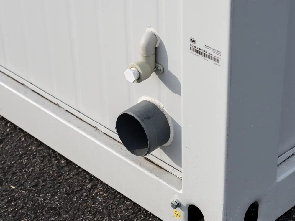 Detailfoto der Wasseranschlüsse eines Sanitärcontainers mit 3/4 Zoll Wasseranschluss und DIN 100 Abwasseranschluss.