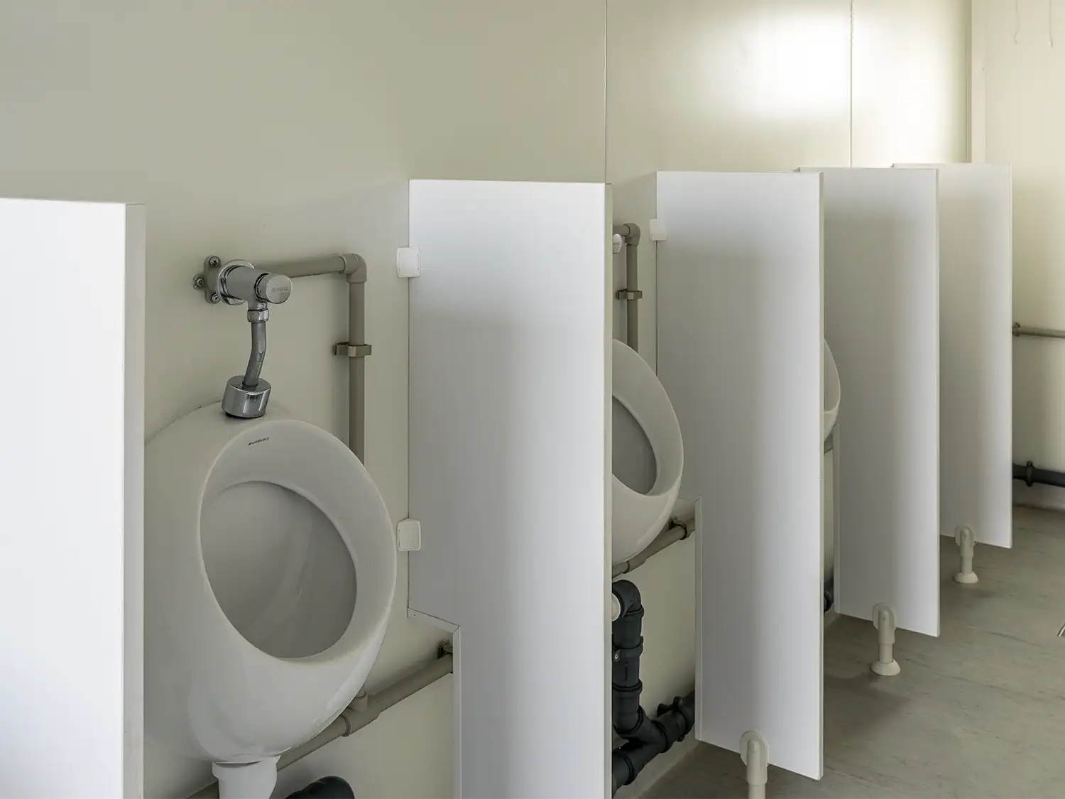 Innenansicht eines Sanitär-WC-Containers mit vier Urinalen bzw. Pissoirs samt Schamwänden.