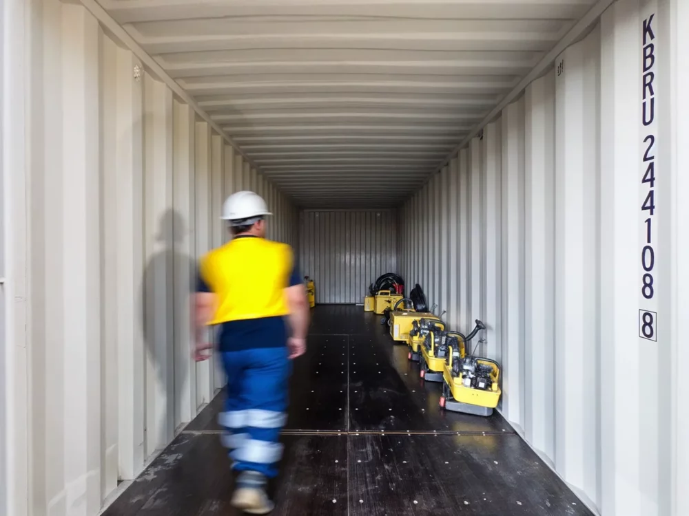 Bauarbeiter welcher in einen gemieteten Schiffscontainer geht um eine Maschine zu lagern.