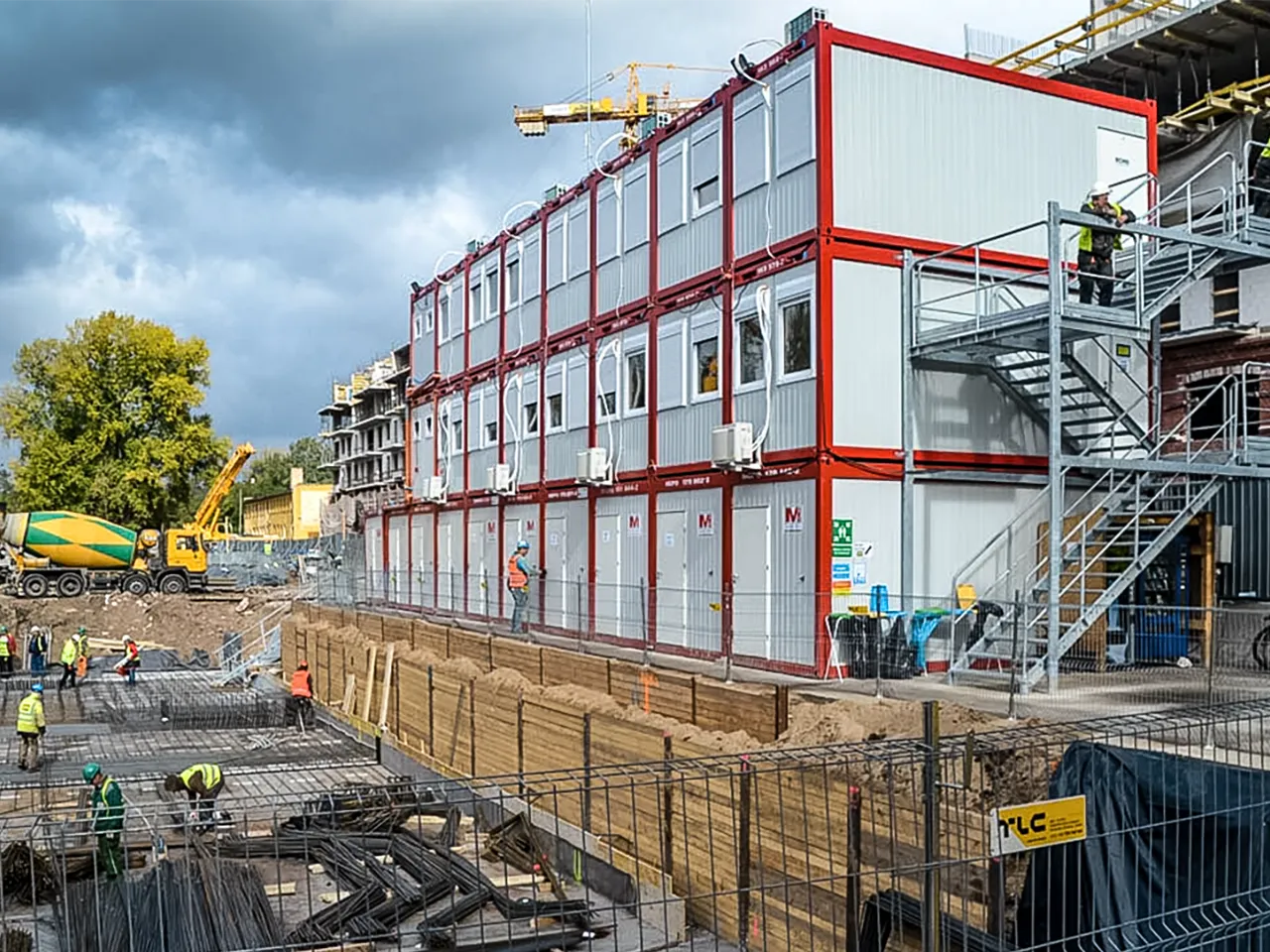 Foto einer Baustelle mit aufgestellten Wohncontainern als dreigeschossige Anlage mit Außentreppe als temporäre Unterkunft für Bauarbeiter.