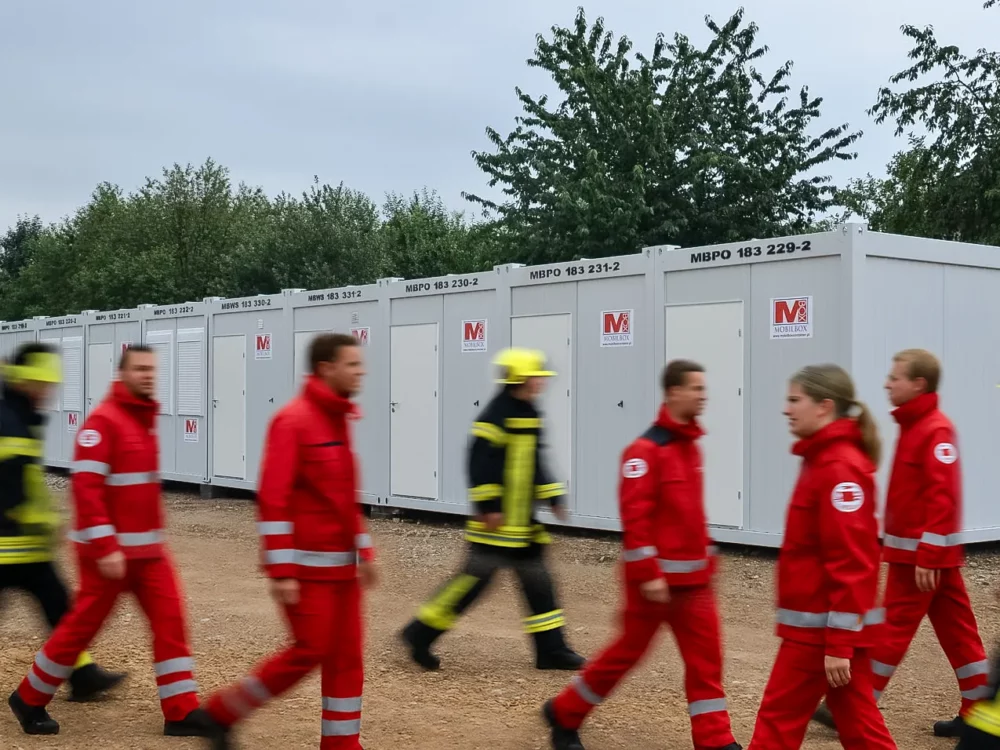 Einsatzkräfte des roten Kreuzes sowie der Feuerwehr welche neben einer gemieteten Wohncontaineranlage im Katastropheneinsatz gehen.