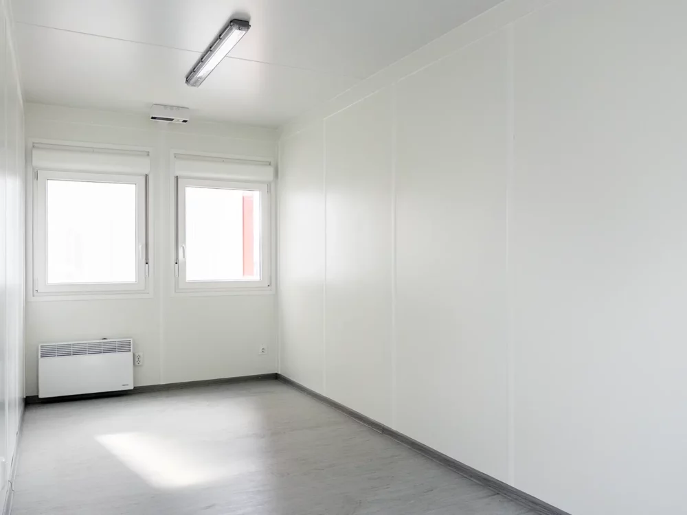 Innenaufnahme eines MB20 Wohncontainers mit weißen Innendekor aus Spanplatten sowie grauem marmorierten PVC-Bodenbelag.
